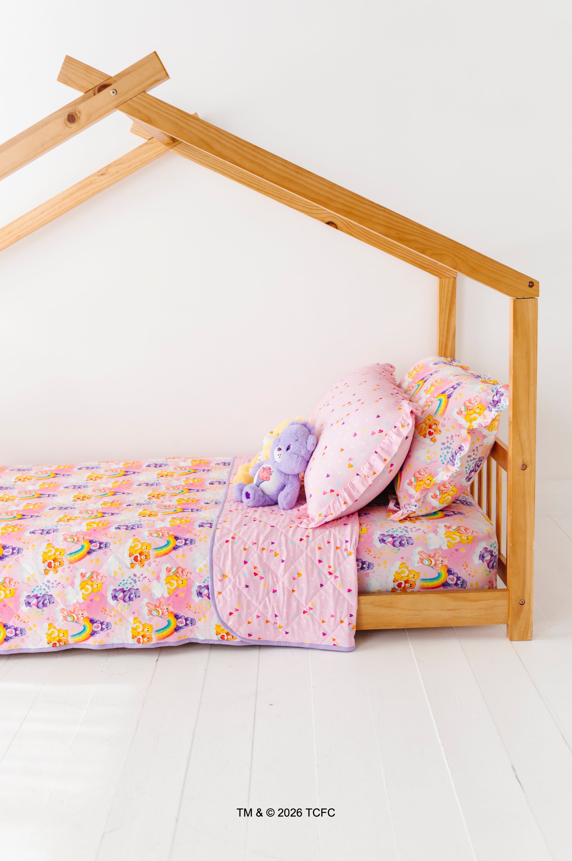 Children's bed with colorful Care Bears™ bedding and a wooden frame on a white floor.