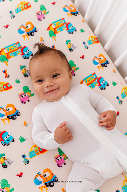 Baby lying on a crib with colorful Leo the Truck bamboo patterned sheets