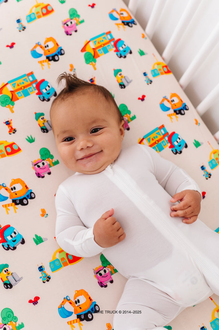 Baby lying on a crib with colorful Leo the Truck bamboo patterned sheets