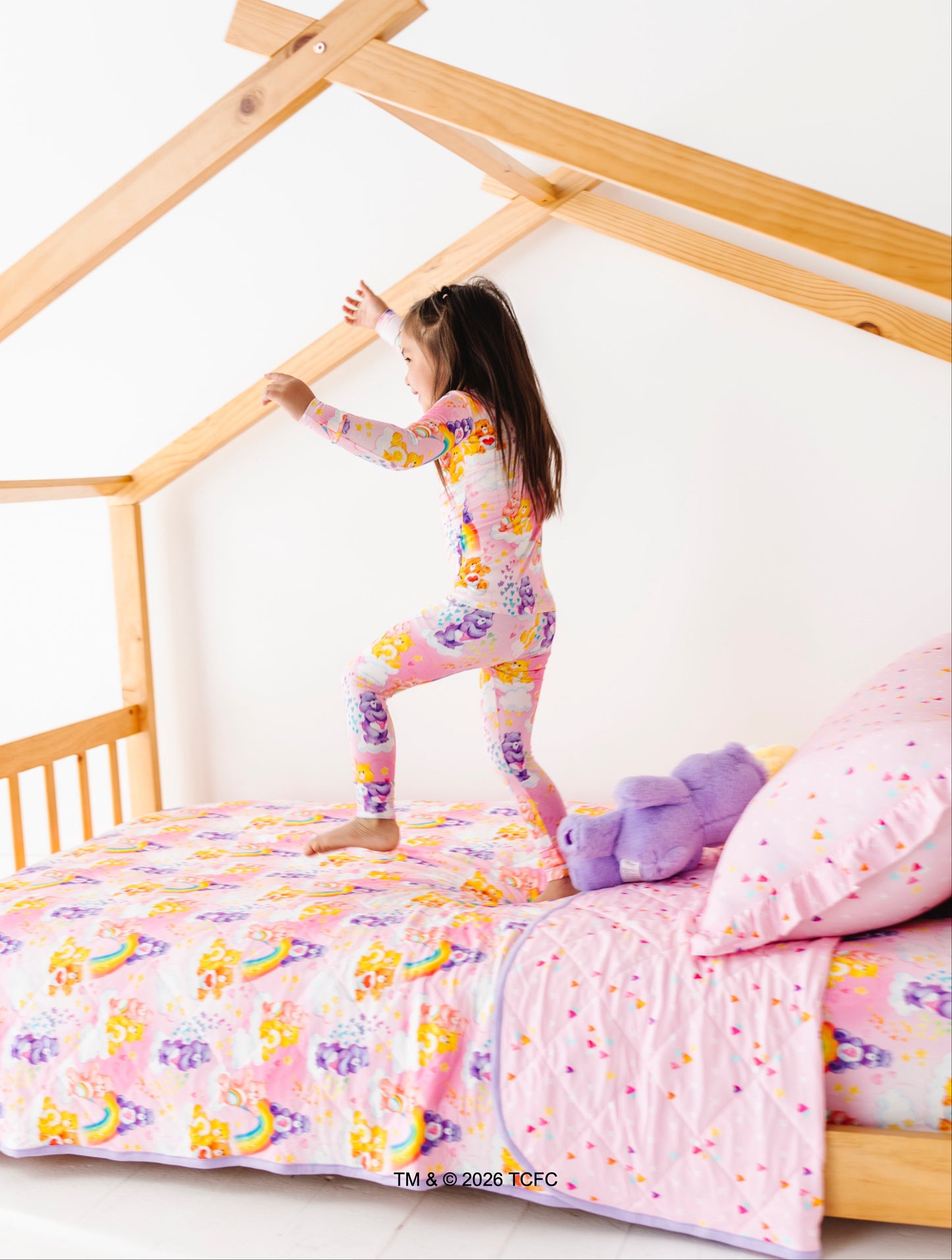 Child playing on a bed with colorful bedding and a wooden house-shaped bed frame.