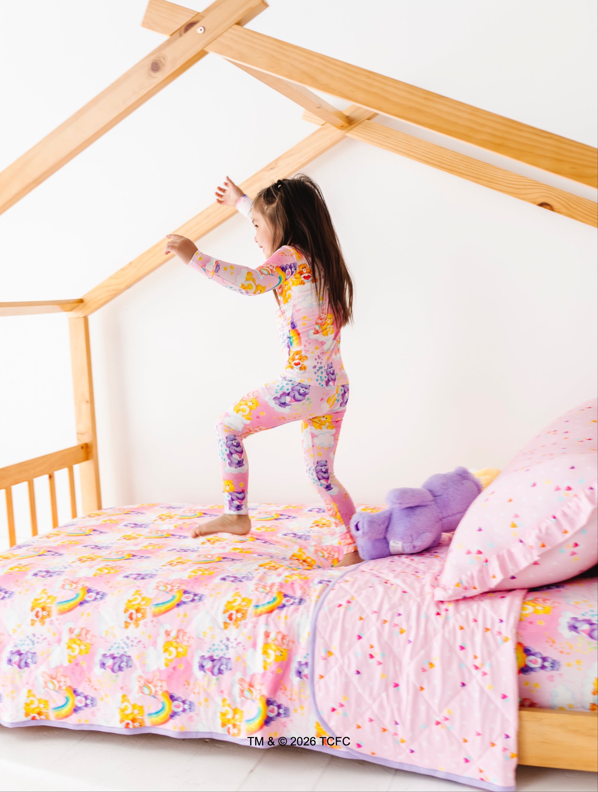Child playing on a bed with colorful bedding and a wooden house-shaped bed frame.