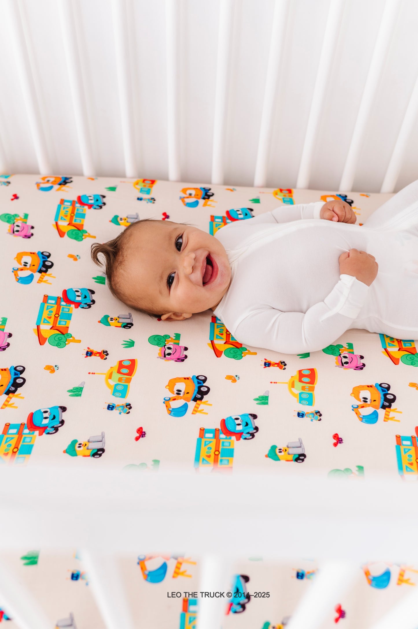 Baby lying on a colorful Leo the Truck bamboo crib sheet 
