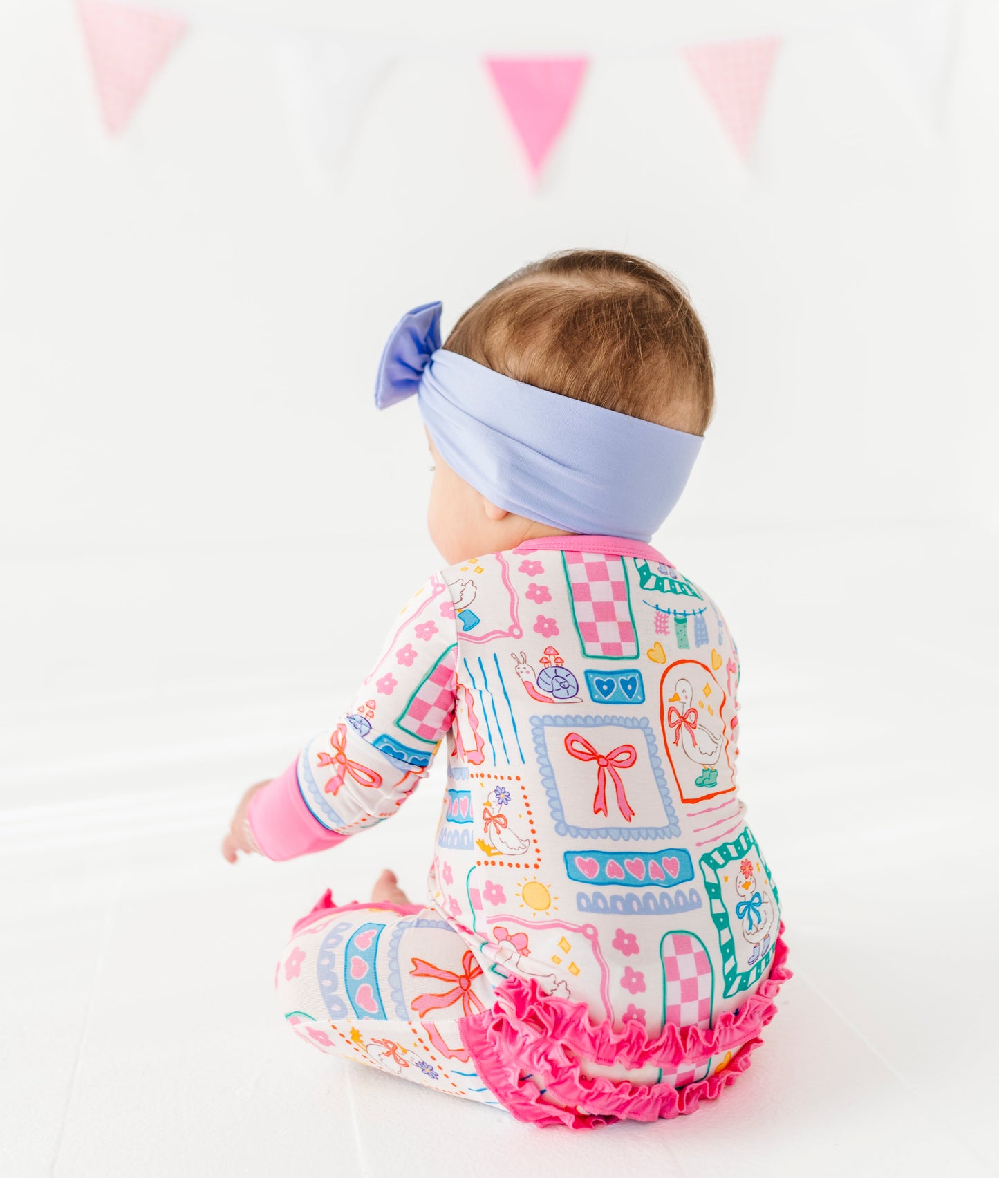 Baby wearing a colorful Geese-patterned romper with ruffles on a white background