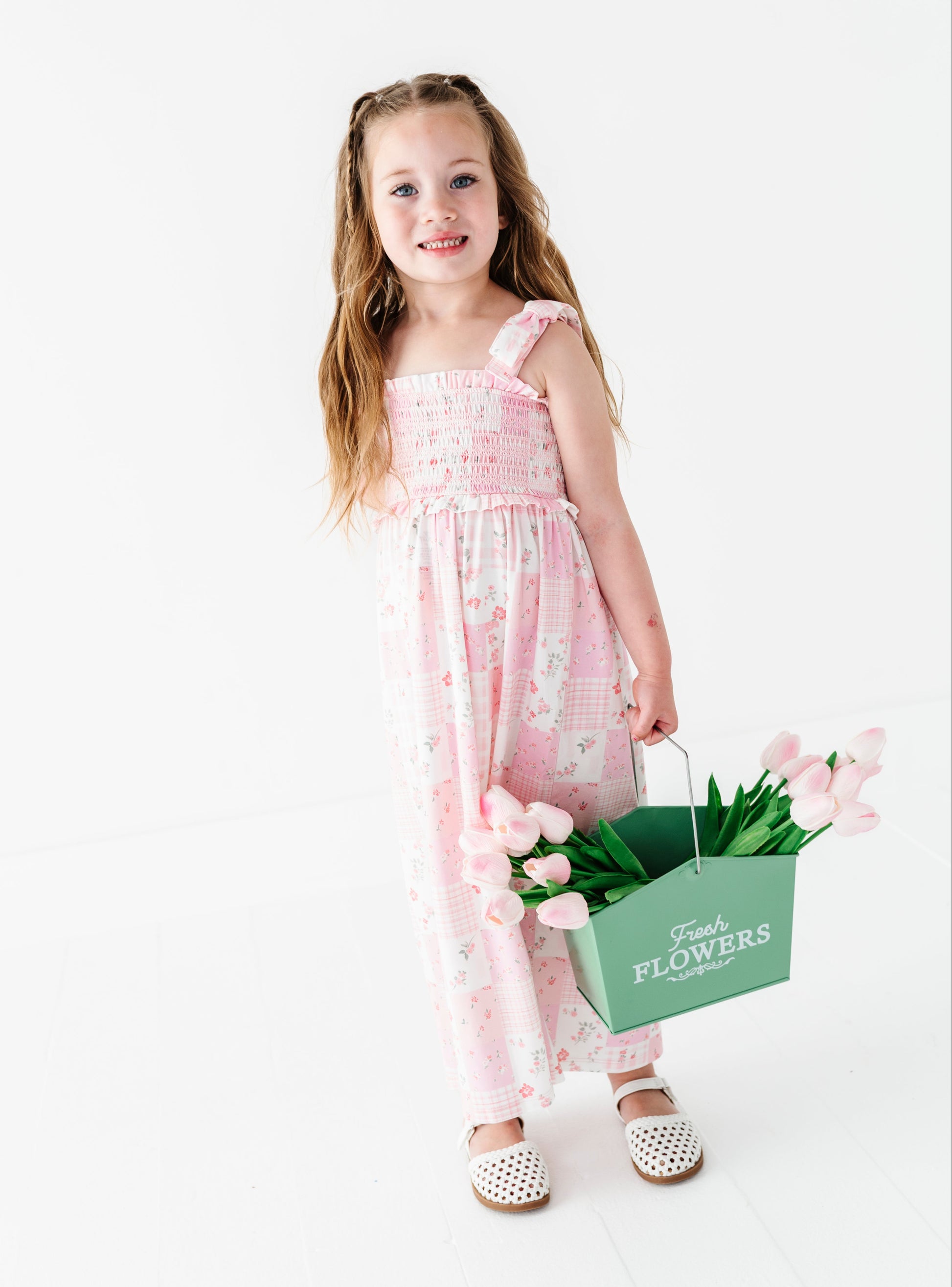 Young girl in a pink floral bamboo maxi dress holding a bouquet of tulips in a green bag on a white background