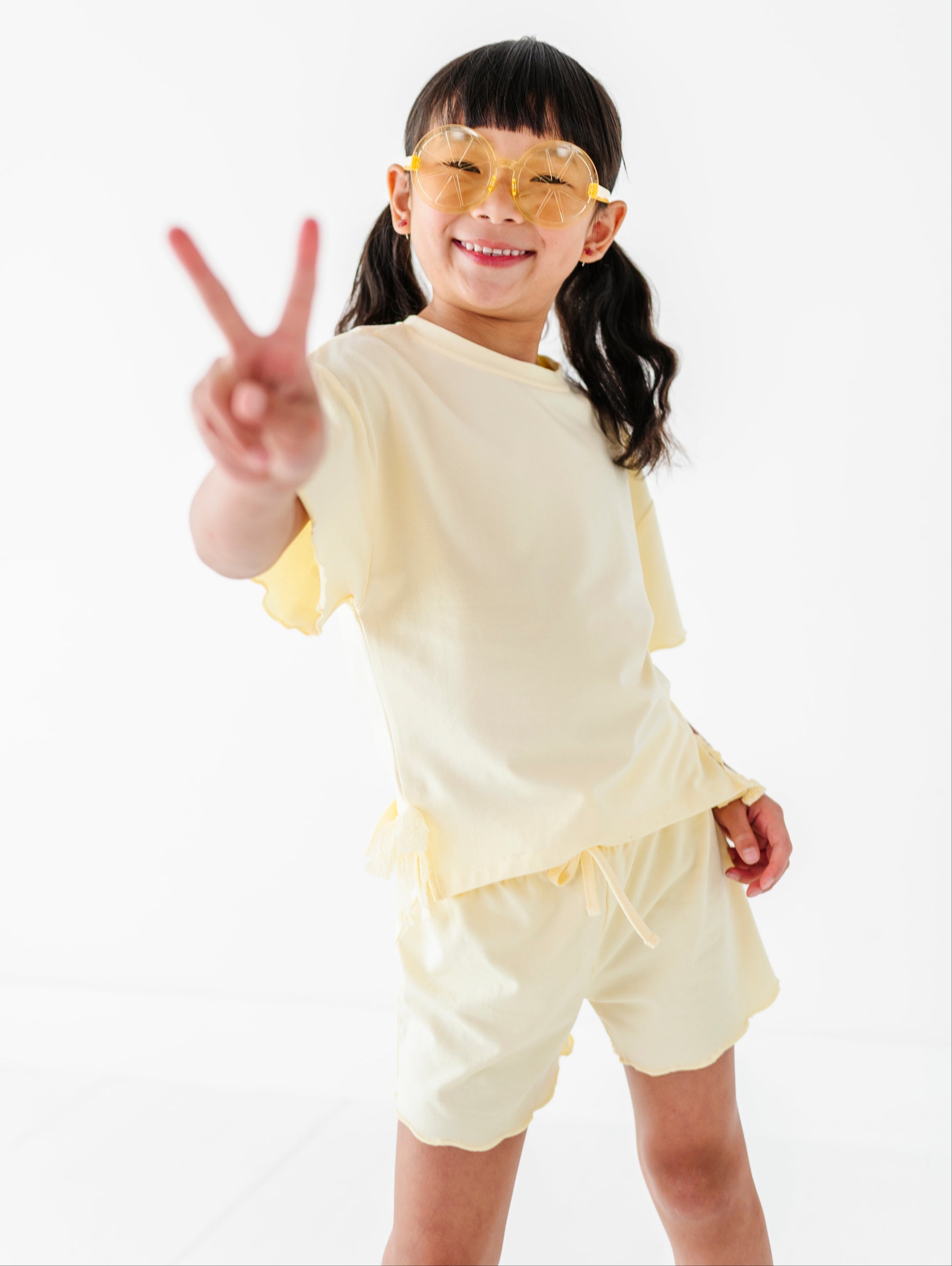 Child in a yellow outfit making a peace sign on a white background