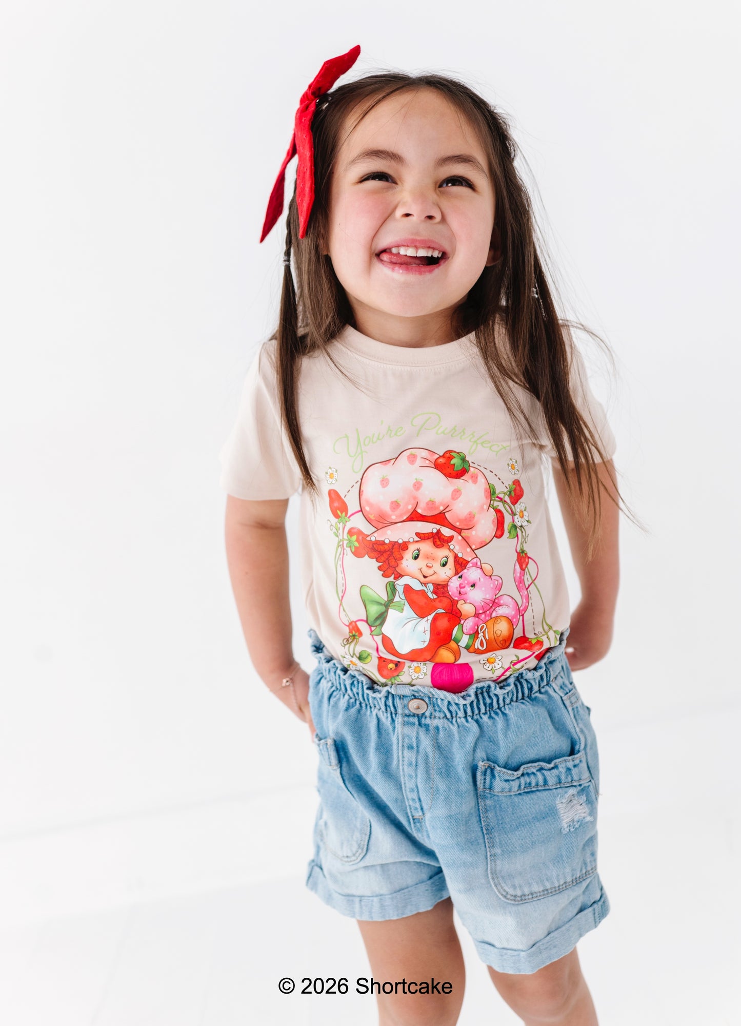 Child wearing an officially licensed Strawberry Shortcake™ t-shirt and denim paperbag shorts on a white background