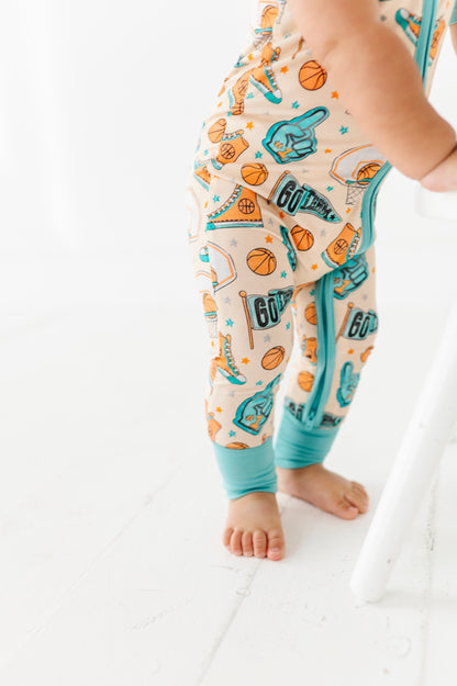 Baby wearing a onesie with sports-themed design on a white floor.
