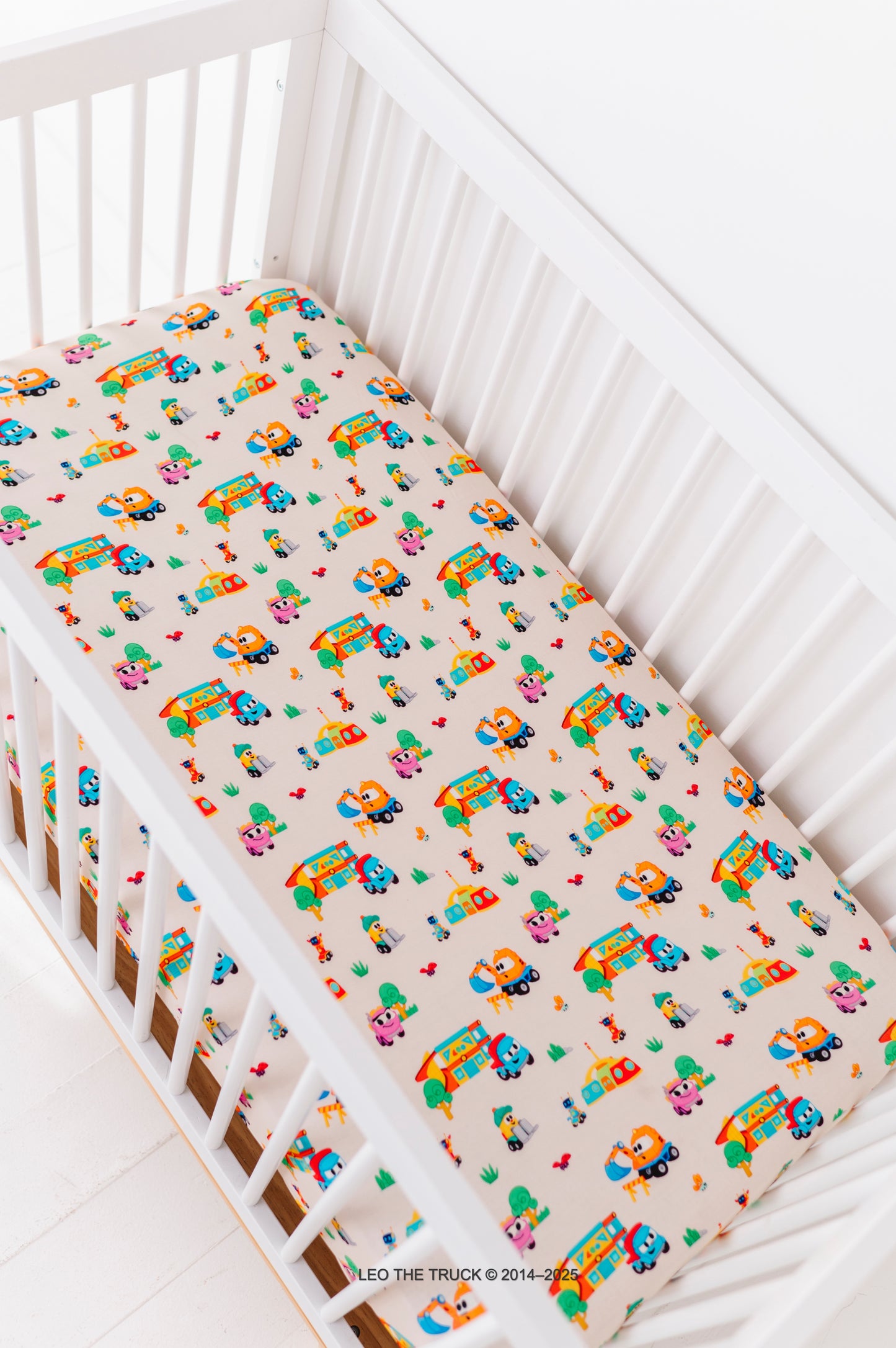 Crib with colorful Leo the Truck truck patterned fitted bamboo sheet on a white background