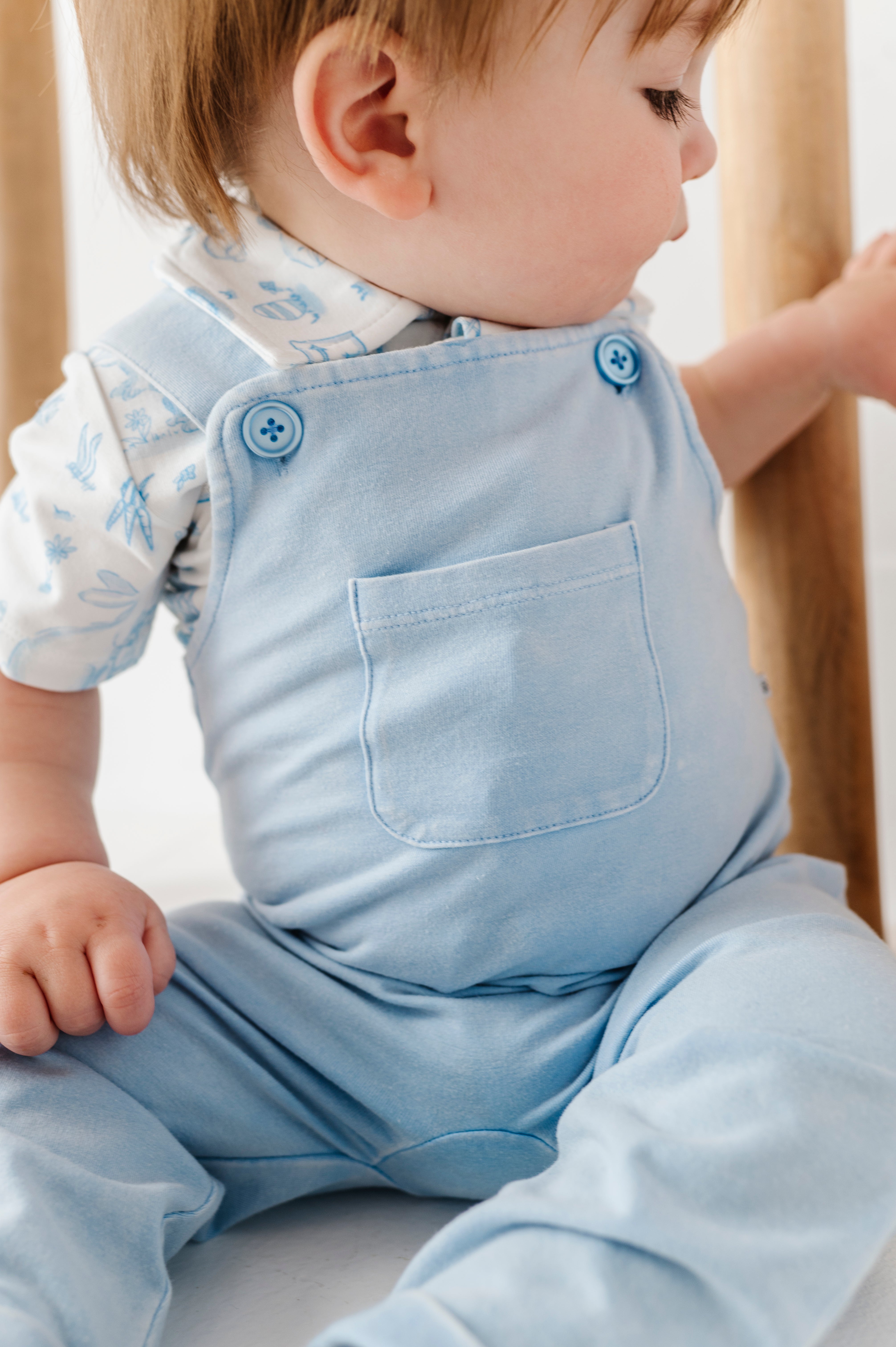 Baby wearing light blue overalls sitting on a white surface.