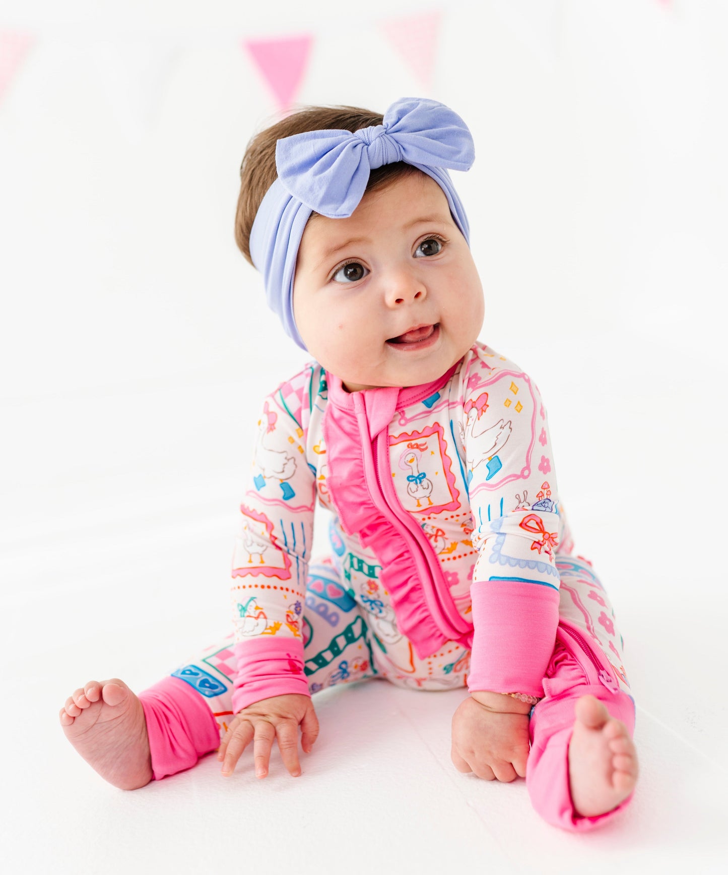 Baby wearing a colorful bamboo romper with pink accents and a headband on a white background
