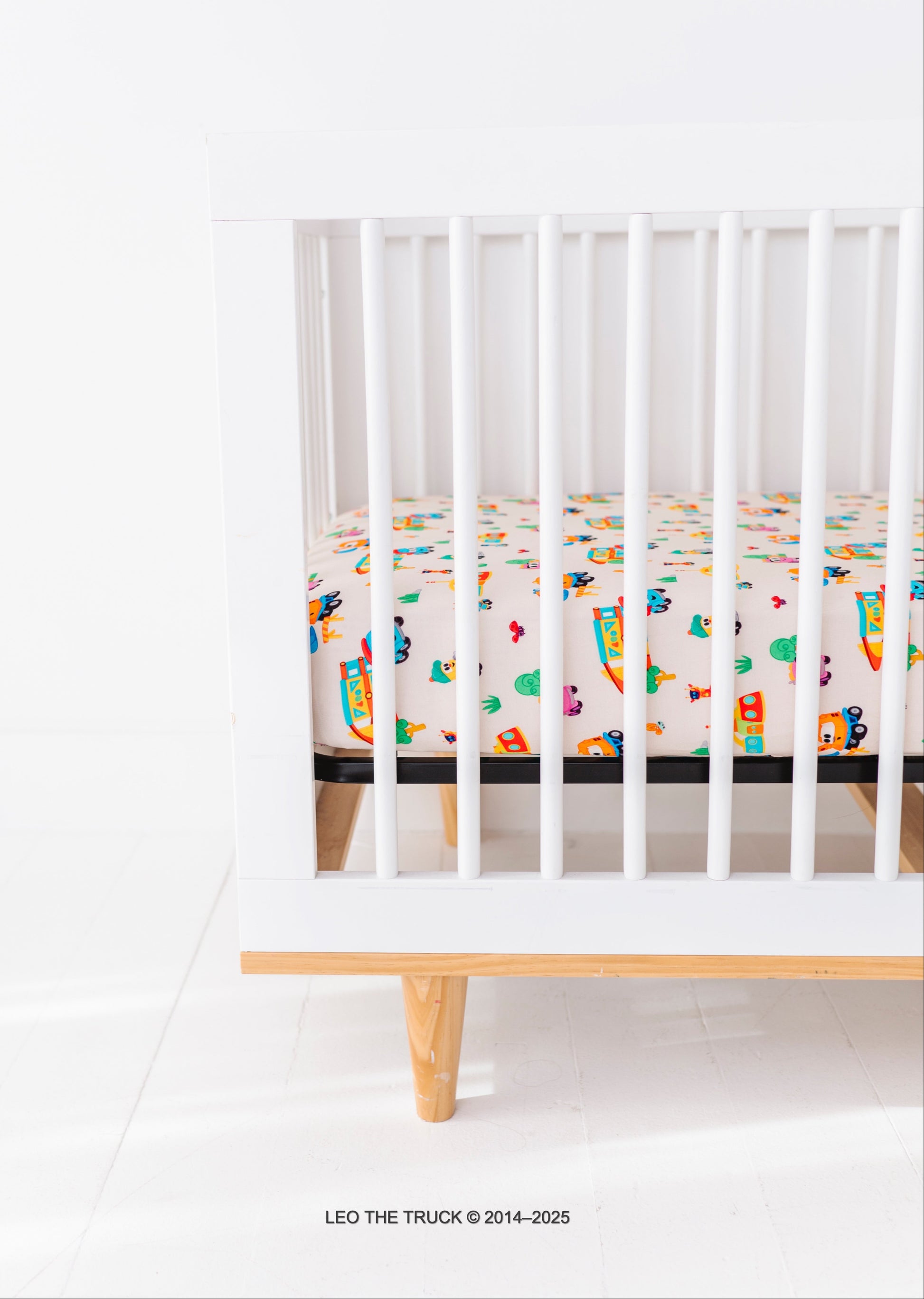 White crib with colorful Leo the Truck bamboo bedding on a white background