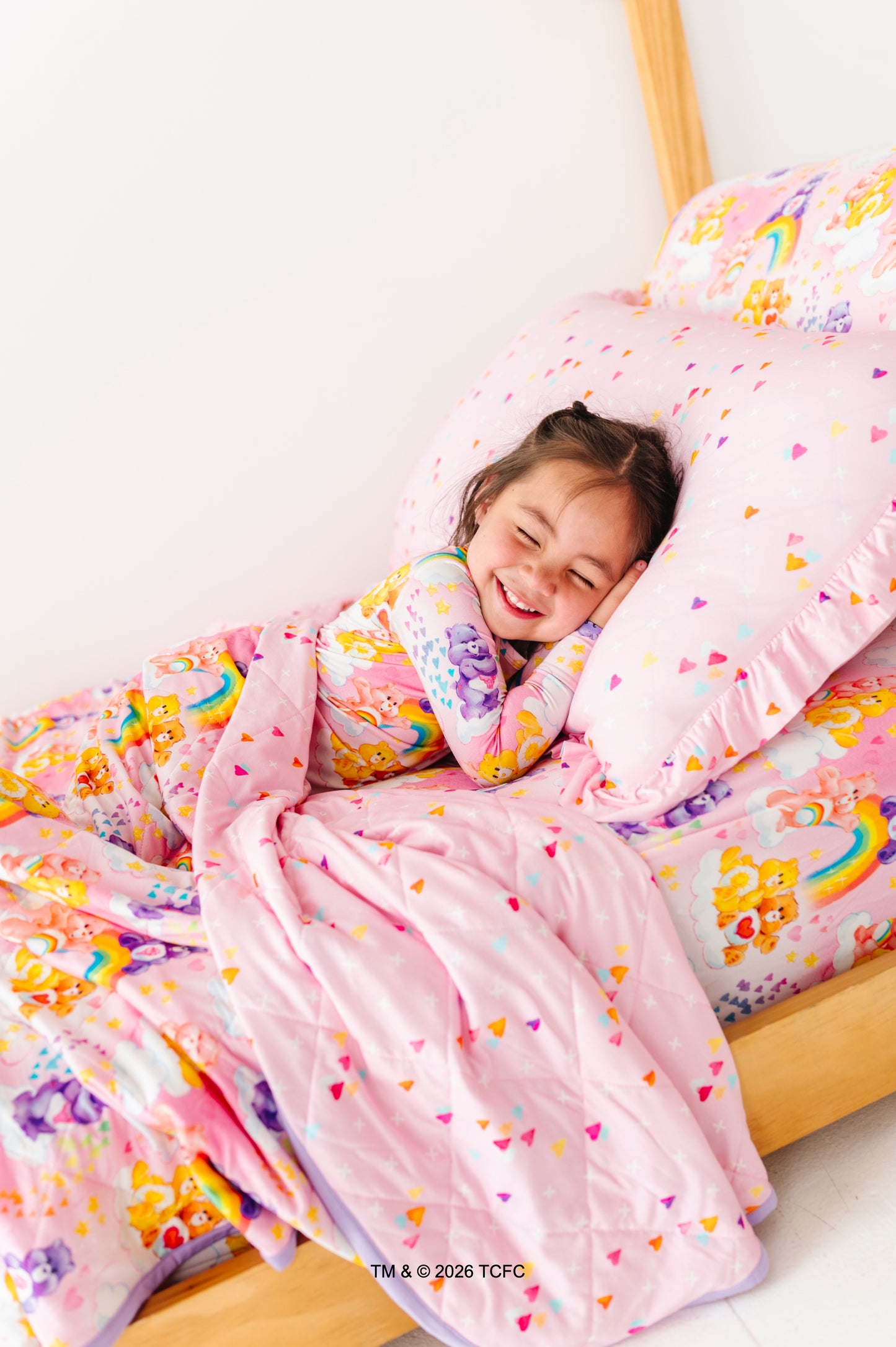 Child lying in bed under colorful bamboo bedding with a smile on a white background