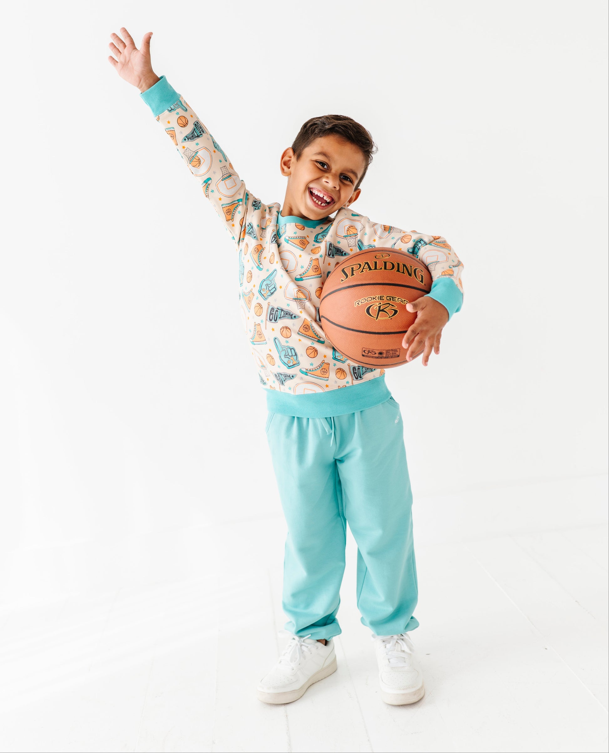 Child holding a basketball with one arm raised wearing a bamboo crewneck featuring a basketball print