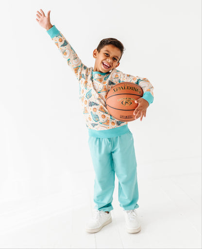Child holding a basketball with one arm raised wearing a bamboo crewneck featuring a basketball print