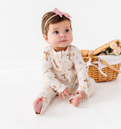 Baby in floral bamboo Easter pajamas sitting on a white surface with a wicker basket in the background.