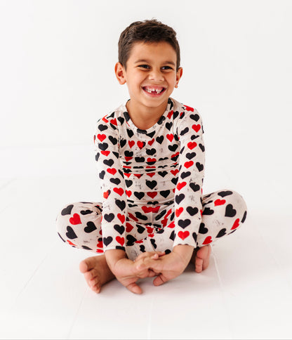 Child sitting cross-legged in King of Hearts bamboo pajamas on white background