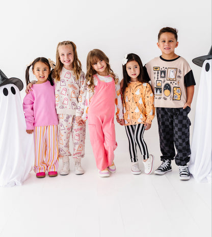 Five children standing together in a studio wearing colorful patterned pajamas and casual outfits, flanked by ghost decorations on a clean white background.
