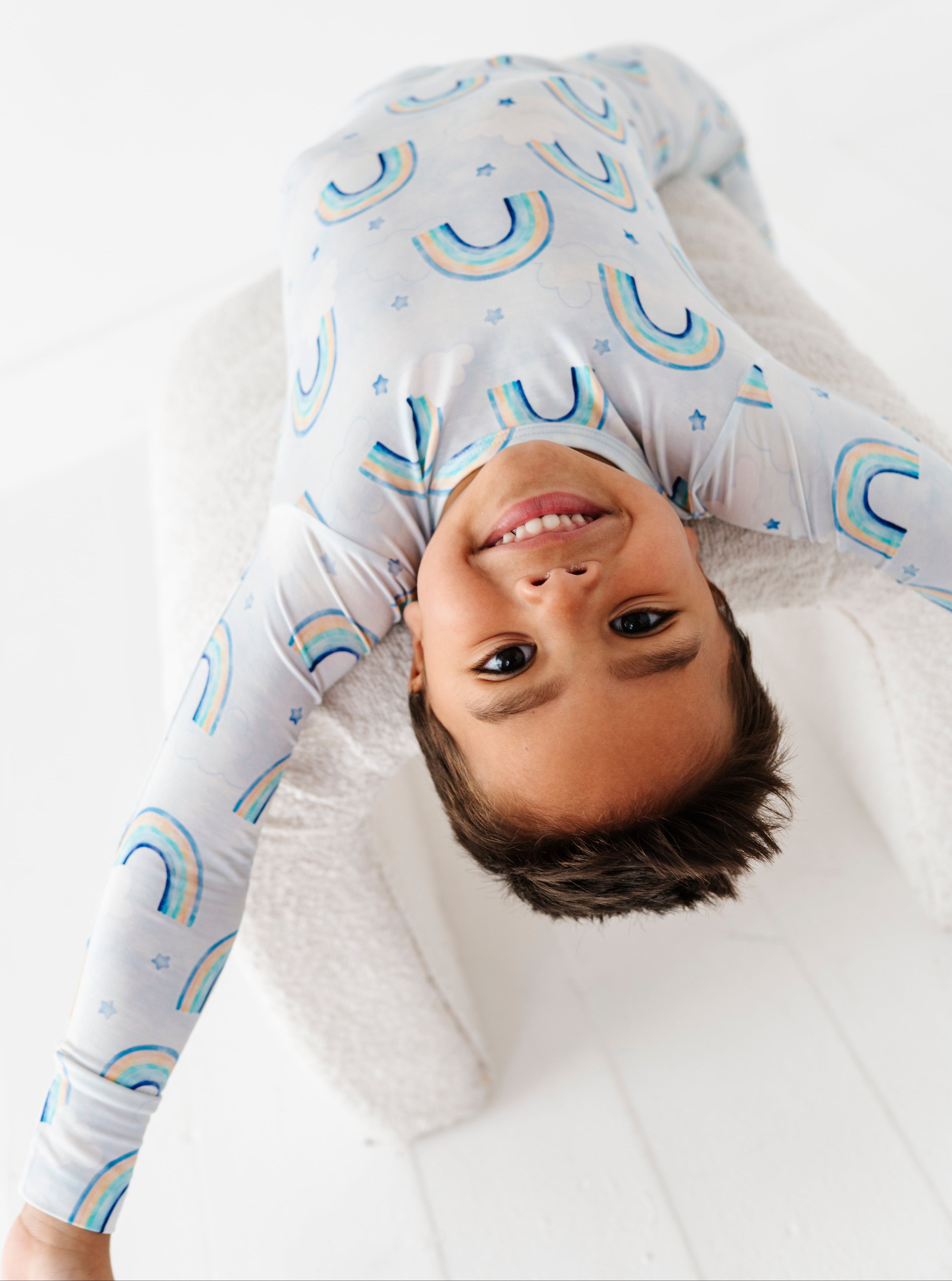 Child wearing a long-sleeve bamboo pj set with rainbow pattern on a white background