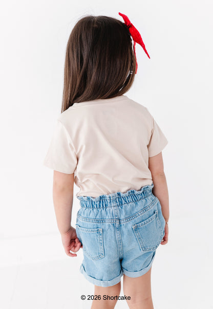Child wearing a beige Strawberry Shortcake™ shirt and denim shorts on a white background