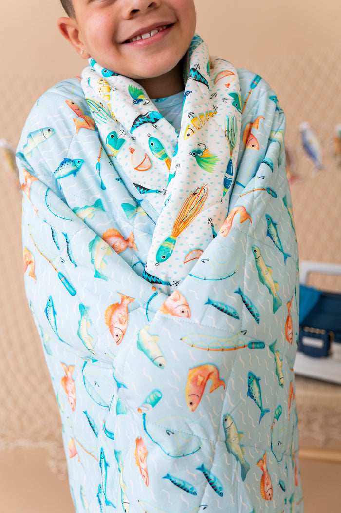 Child wrapped in a colorful fish-patterned bamboo blanket with a neutral background