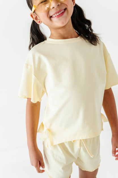 Young girl wearing a light yellow outfit with a plain background