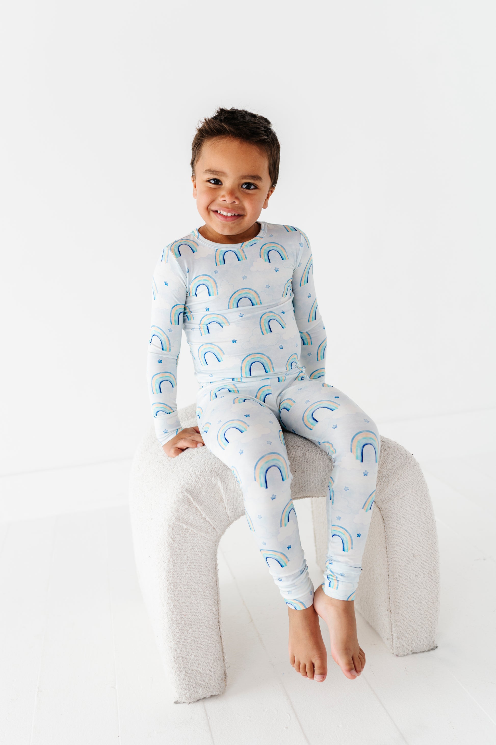 Child wearing a bamboo long-sleeve shirt and pant pajama set with blue watercolor rainbows on a white background