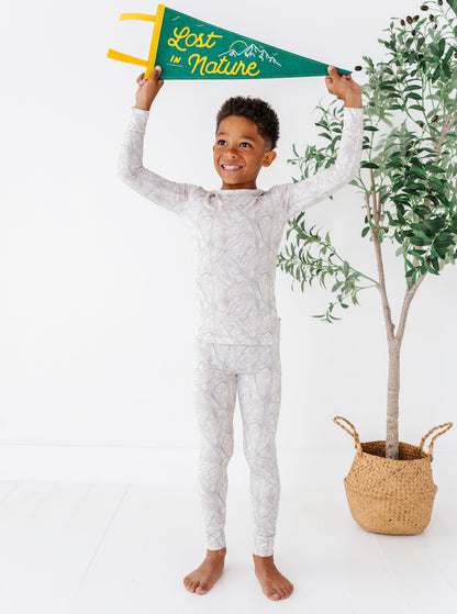 Child in tree camo patterned pajamas holding a 'Lost in Nature' flag with a plant in the background.