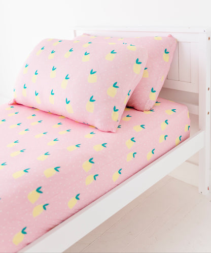Pink bed sheets with lemon pattern on a white bed frame.