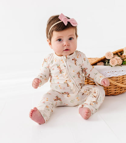 Baby wearing a floral bamboo convertible romper sitting on a white surface with a basket of flowers in the background.