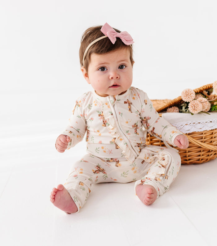 Baby wearing a floral bamboo convertible romper sitting on a white surface with a basket of flowers in the background.