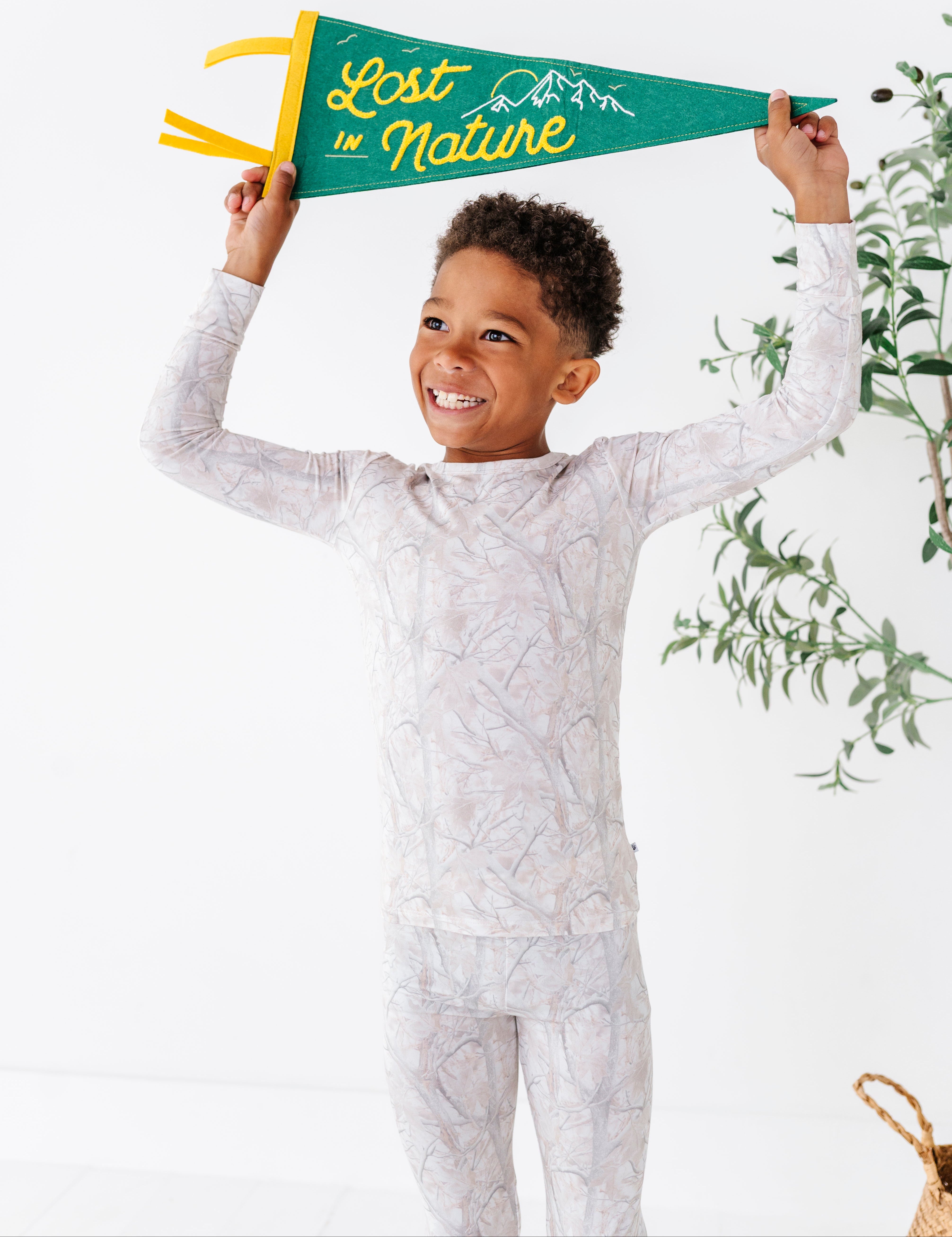 Child wearing a patterned outfit holding a 'Lost in Nature' banner against a white background with greenery.