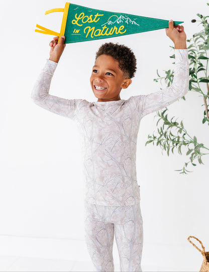 Child wearing a patterned outfit holding a 'Lost in Nature' banner against a white background with greenery.