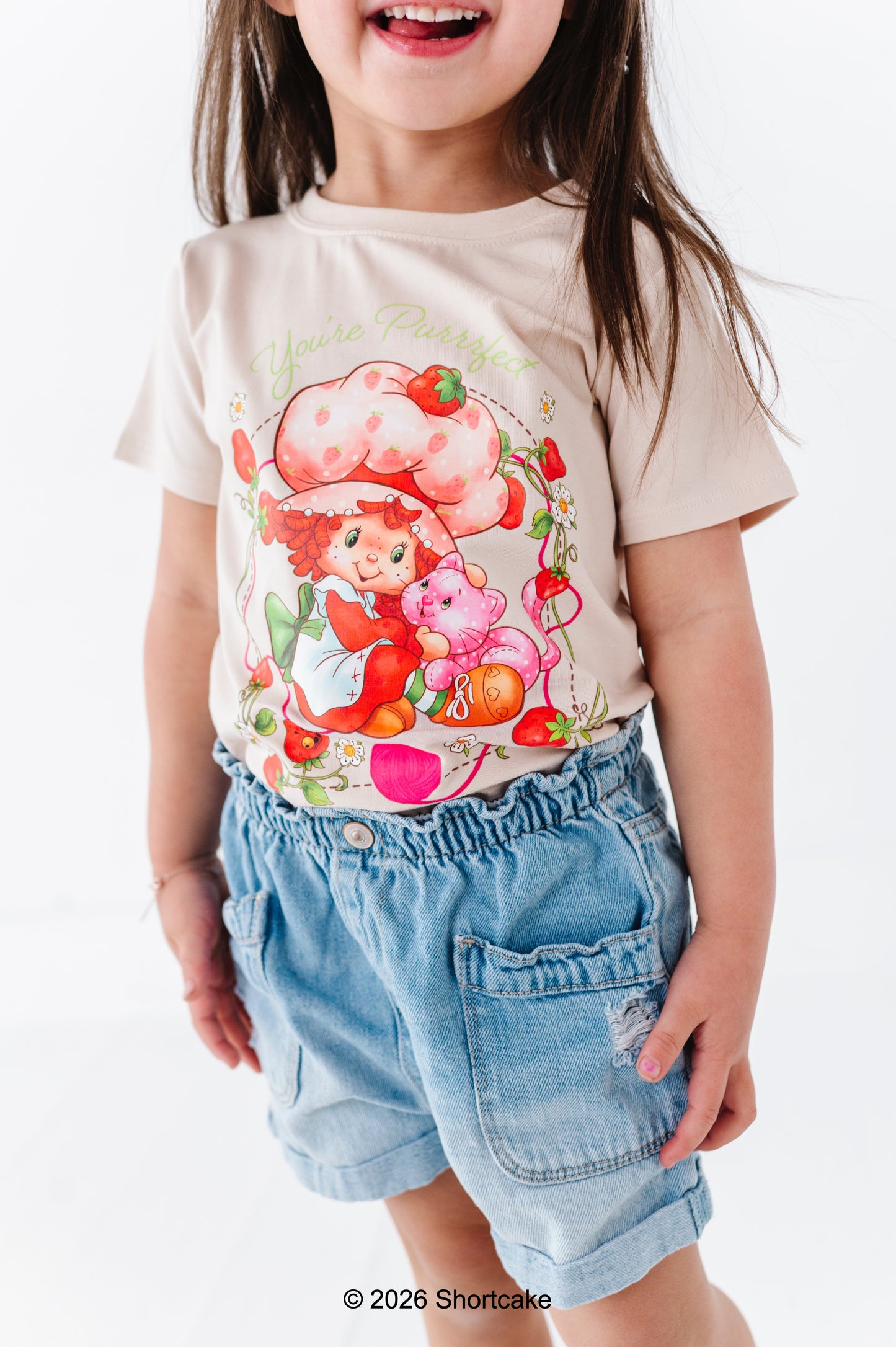 Child wearing a Strawberry Shortcake™ bamboo cotton graphic tee and denim shorts on a white background