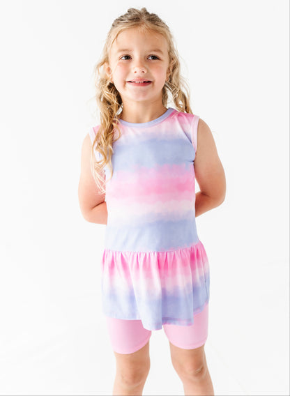Young girl wearing a tie-dye bamboo-cotton peplum top with pink and blue gradient on a white background