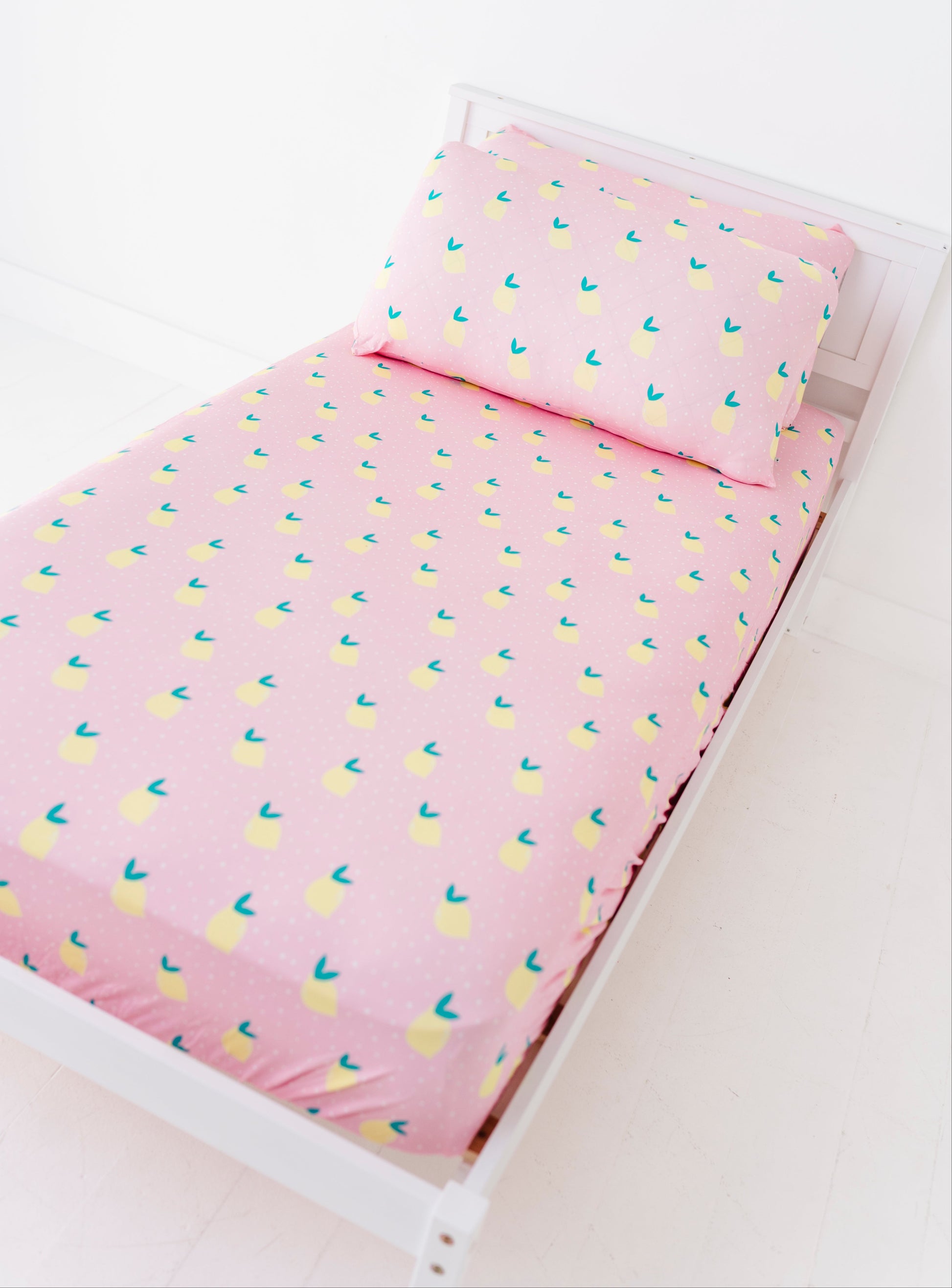 Pink bed sheet with lemon pattern on a white bed frame