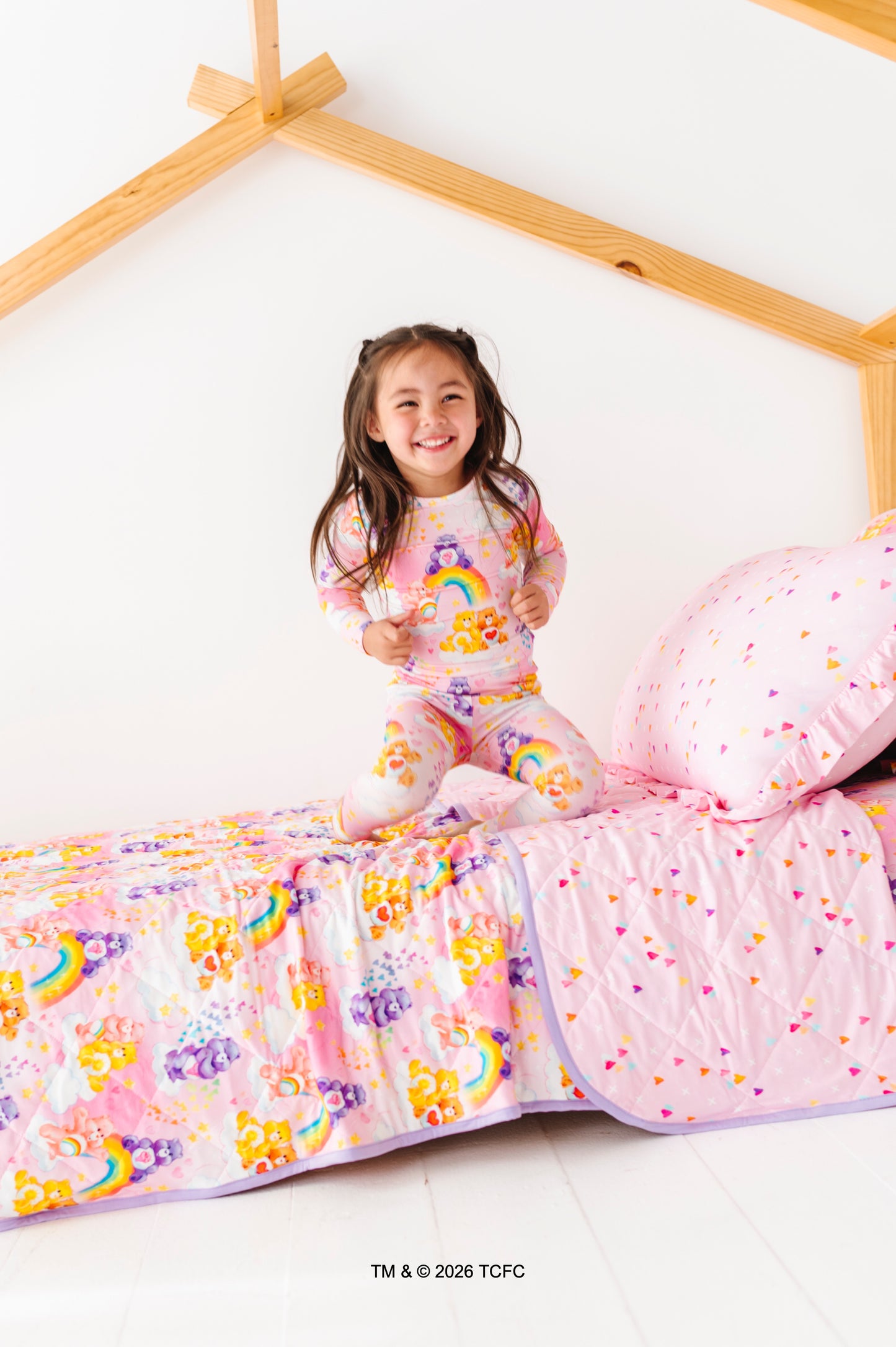 Child in Care Bears™ pajamas bouncing on a bed featuring matching Care Bears™ bedding 