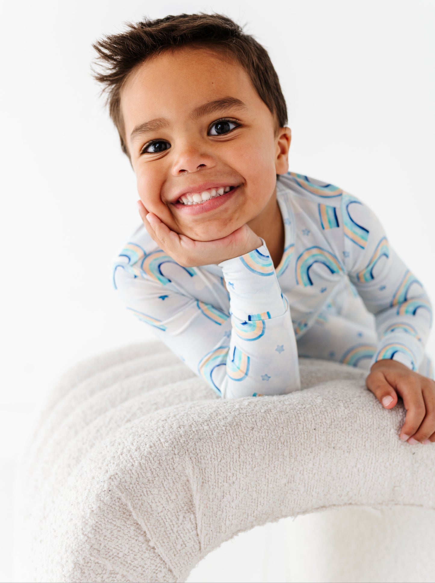 Child wearing a two-piece bamboo pajama set with blue rainbows, sitting on a white surface.