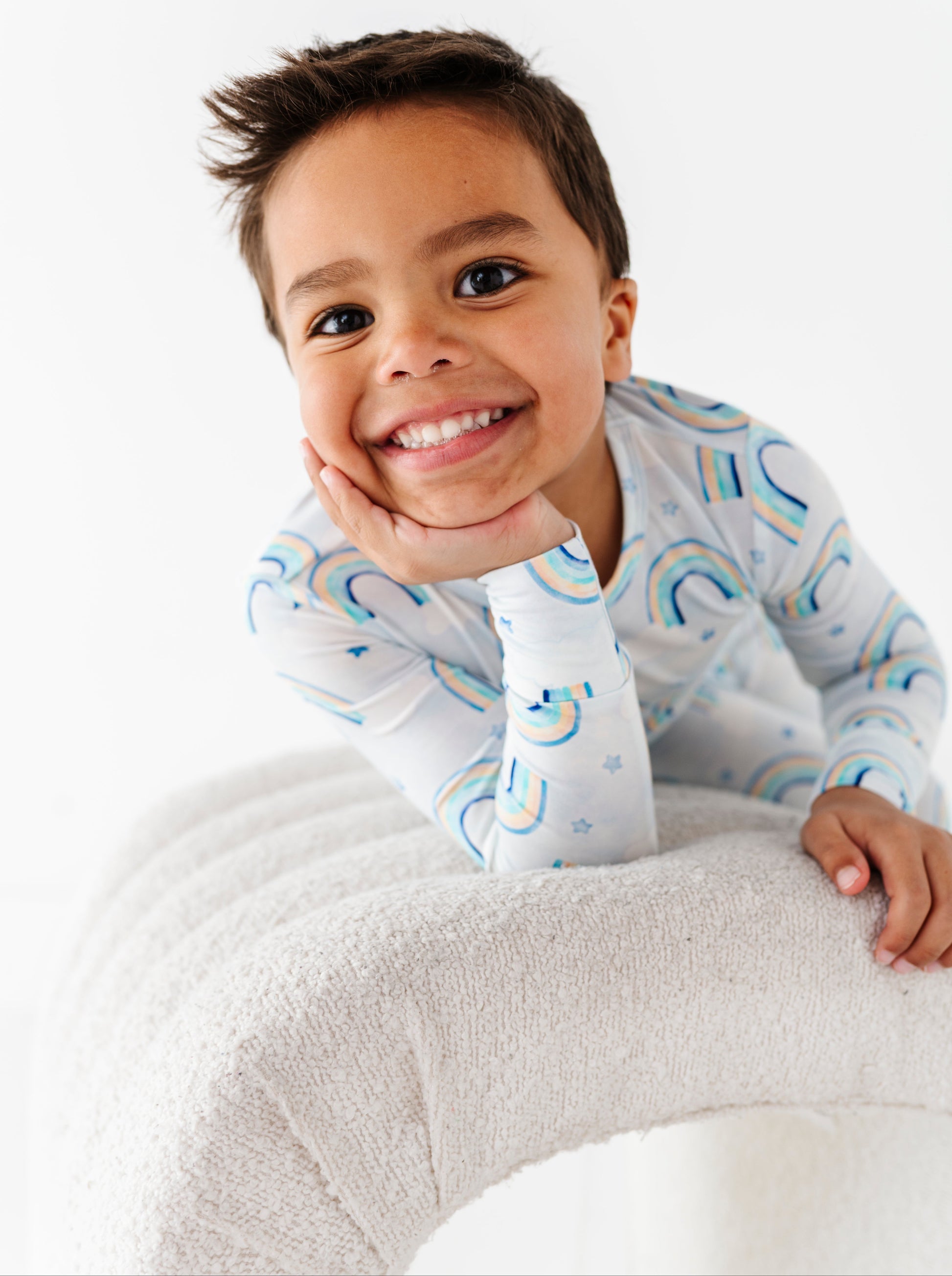 Child wearing a two-piece bamboo pajama set with blue rainbows, sitting on a white surface.