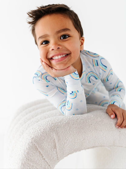Child wearing a two-piece bamboo pajama set with blue rainbows, sitting on a white surface.