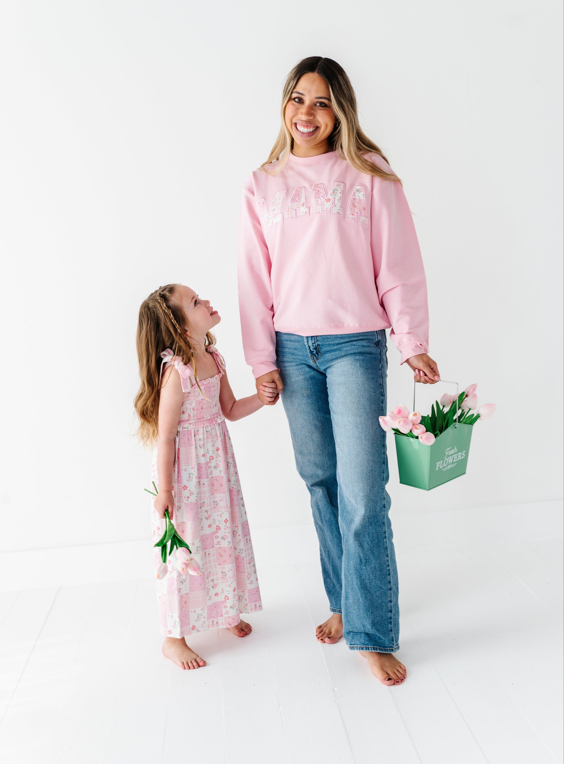 Mom and young girl holding hands in matching bamboo outfits with a flower basket on a white background