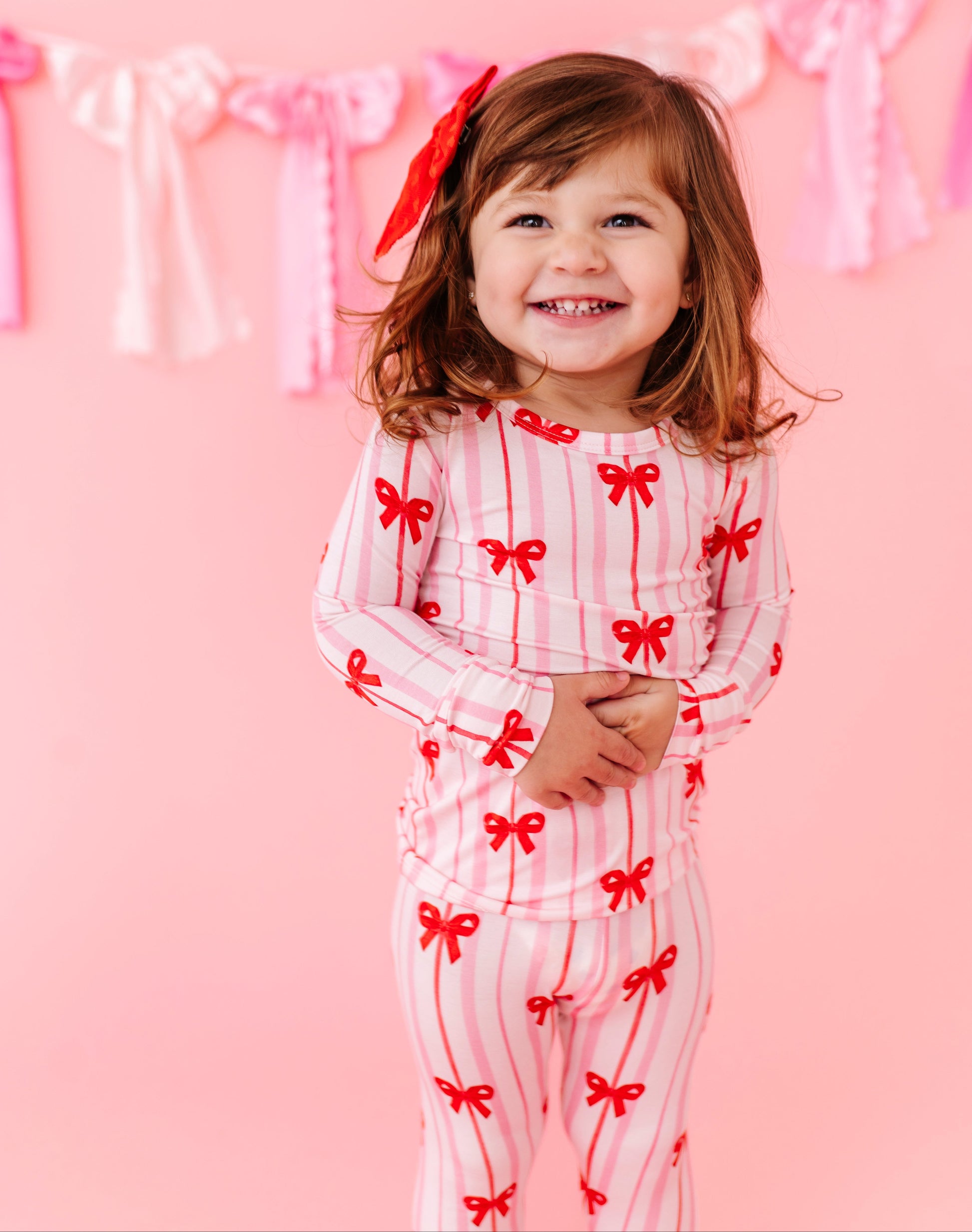 Toddler wearing Ruby Ribbons bamboo pajamas with red bow print and pink stripes