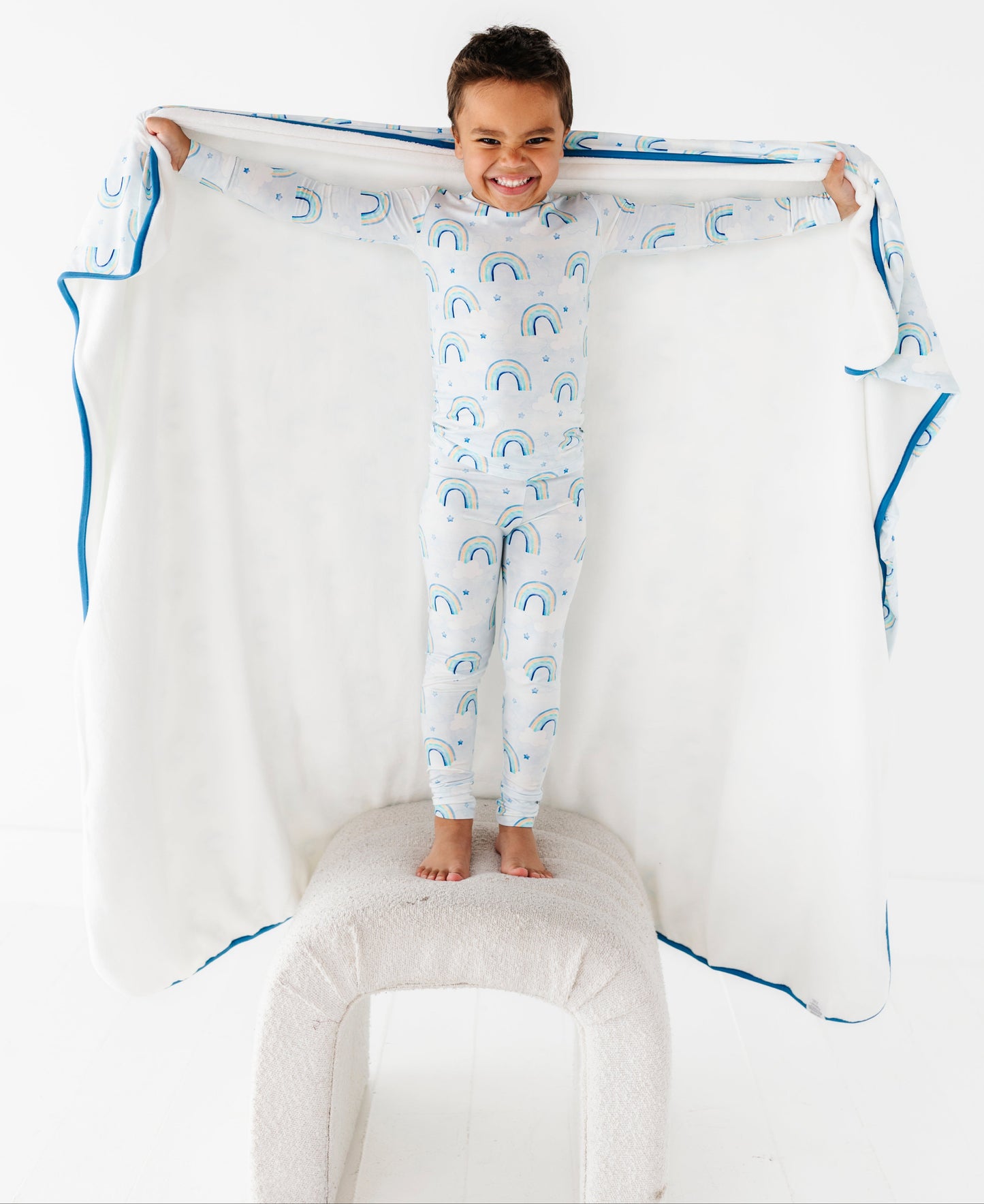 Child in a bamboo two-piece pajama set with cloud pattern holding a large matching blanket with blue trim on a white background