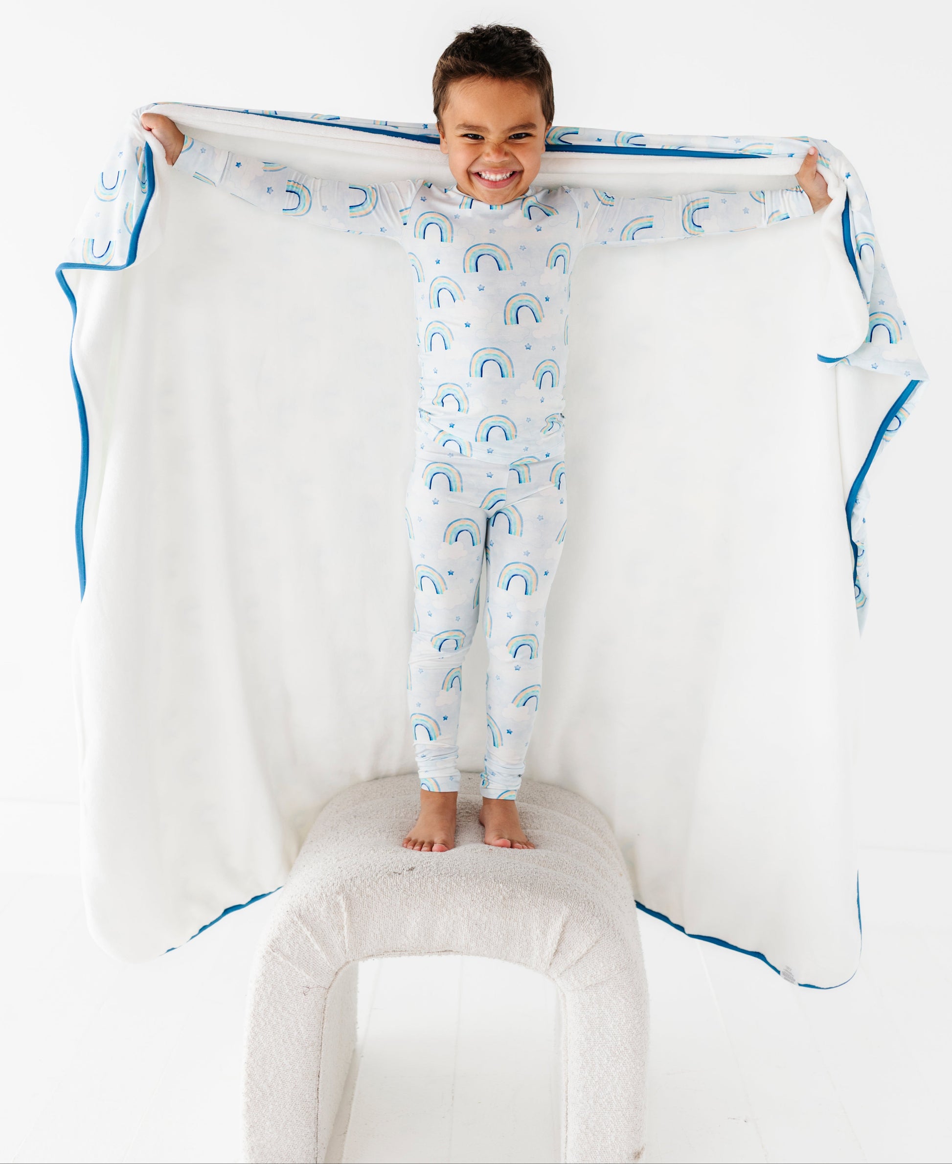 Child in a bamboo two-piece pajama set with cloud pattern holding a large matching blanket with blue trim on a white background