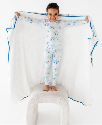 Child in a bamboo two-piece pajama set with cloud pattern holding a large matching blanket with blue trim on a white background