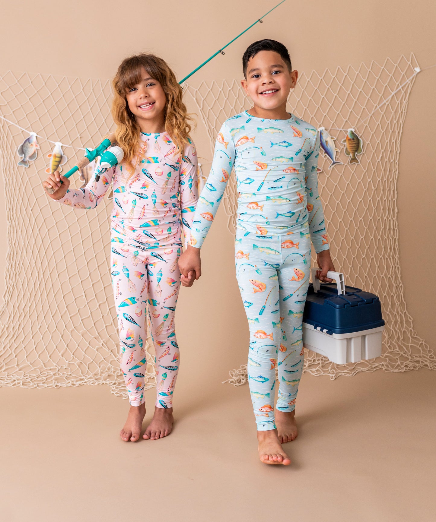 Two children wearing matching pajamas with fishing patterns, standing against a beige background.