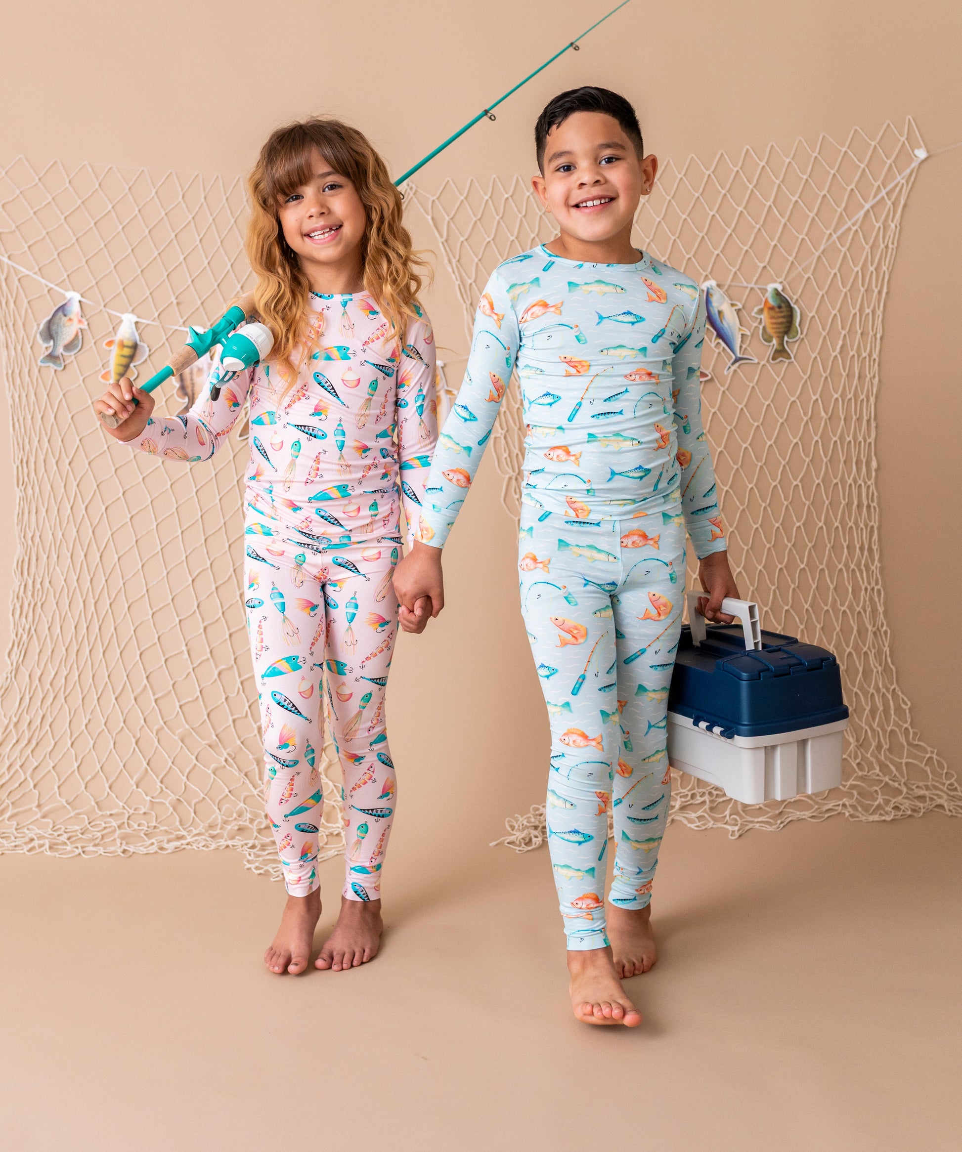 Two children wearing matching pajamas with fishing patterns, standing against a beige background.