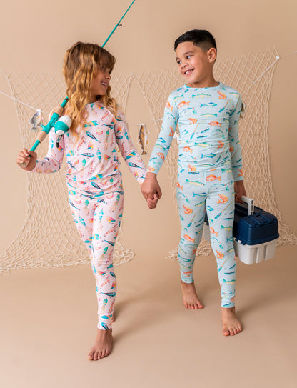 Two children in matching pajamas with fishing-themed designs, holding fishing equipment.