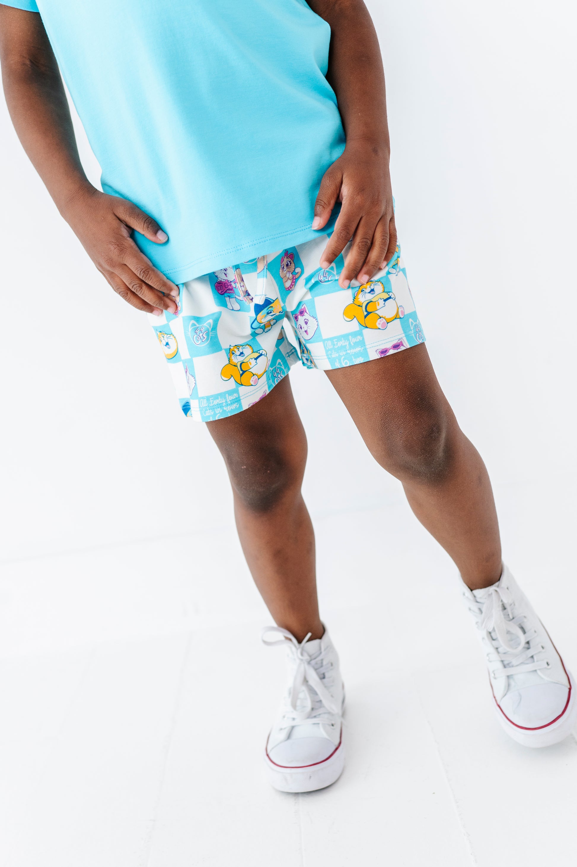 Little boy wearing light blue short sleeve shirt and 44 Cats bamboo blend shorts on a white background