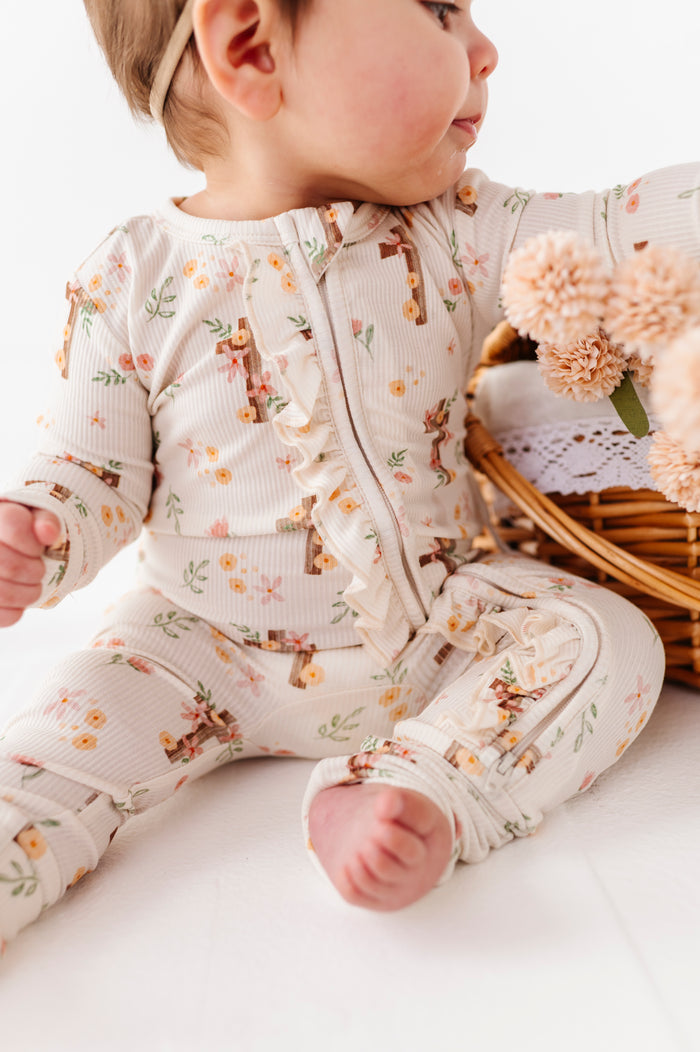 Baby in a floral bamboo onesie sitting next to a basket of flowers on a white surface