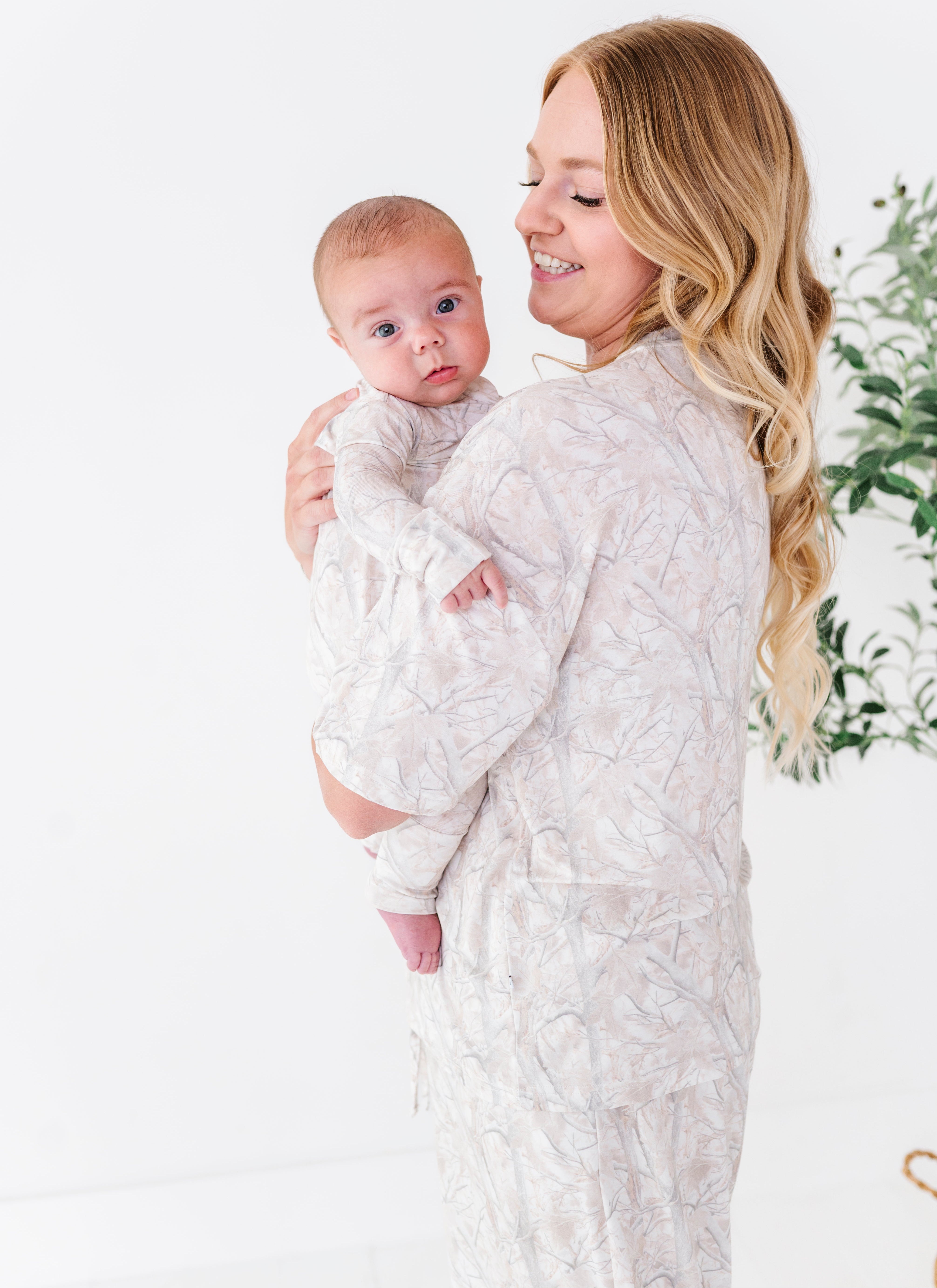 Woman holding a baby wearing a tree camo romper against a white background